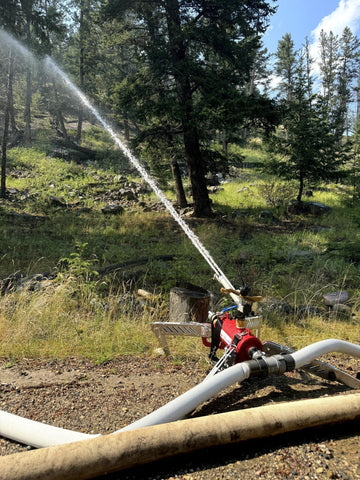 FireBozz wildfire sprinkler in operation near homes with dramatic sky and mountainous background